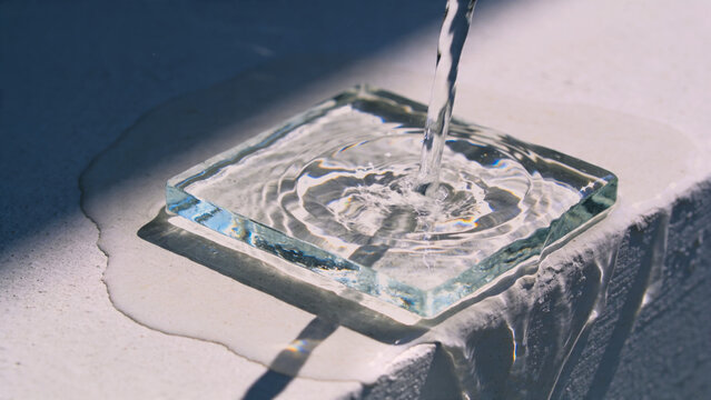 コンクリート質の構造物の上に薄っぺらい氷があり、それにめがけて水が注がれている、