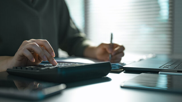 Close-up of accountant calculating budget and writing report beside laptop in modern office, showing finance analysis.