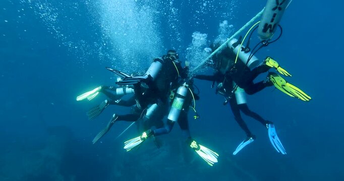 A group of divers diving towards a sunken ship SS Thistlegorm in the Red Sea. Divers descend together into a cloud of bubbles  around a guide rope. Summer vacation shot