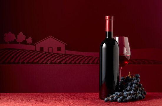 Bottle and glass of red wine with blue grapes on a red background.