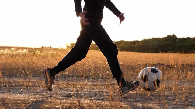 Young boy dribbling soccer ball through golden rural field at sunset. Child practicing football alone outdoors in countryside. Healthy childhood, training and freedom concept. Sports childhood.