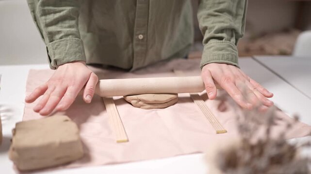 Artist Rolling Clay Slab with Rolling Pin 4K Video Slow Motion. Artist uses a wooden rolling pin to flatten raw earthenware clay into a uniform slab for ceramic artwork