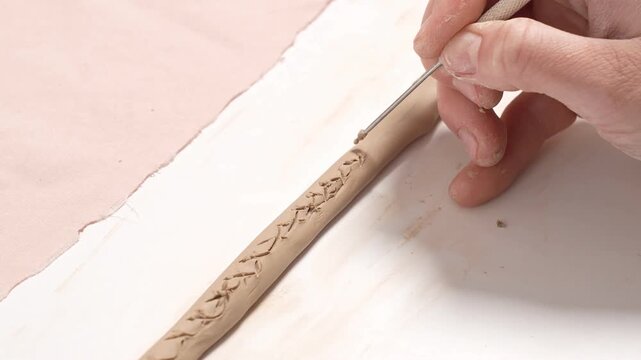 Artist uses a sharp metal carving tool to incise a repeating decorative texture into the curved wall of a clay artwork. Artisan Carving Clay Texture with Tool 4K Video Slow Motion