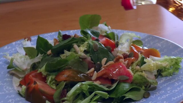 Freshly made salad with tomatoes, nuts, and seeds getting seasoned with apple cider vinegar