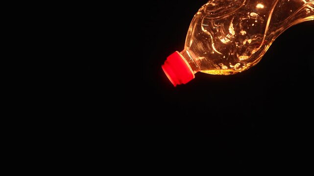 Bright golden vegetable oil pouring from plastic bottle with dramatic warm lighting on black background. Food cooking ingredient concept with copy space and glowing reflections.