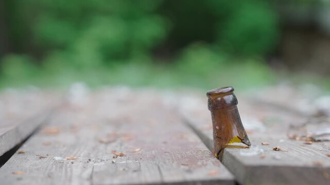 Broken Brown Glass Bottle Neck Stuck in Wooden Picnic Table Outdoors | Slow Parallax Camera Move | Environmental Pollution and Littering Concept