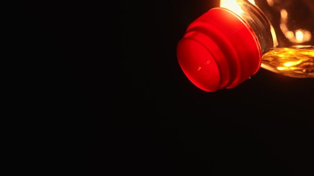 Bright golden vegetable oil pouring from plastic bottle with dramatic warm lighting on black background. Food cooking ingredient concept with copy space and glowing reflections.