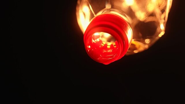 Bright golden vegetable oil pouring from plastic bottle with dramatic warm lighting on black background. Food cooking ingredient concept with copy space and glowing reflections.