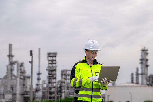 Professional male industrial engineer typing on laptop analyzing system software at petrochemical refinery plant for sustainable corporate oil and gas energy manufacturing business development.