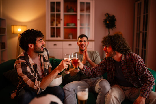 Male friends enjoying beers cheering sports at home