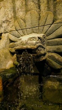The sculpture typically features a snake head emerging from a ring of stylized feathers, often functioning as a fountain.