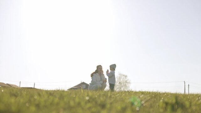 Young mother with her little child playing on a green grassy hill during a sunny spring day, creating a happy family memory while enjoying nature and fresh air together in the countryside. Slow motion