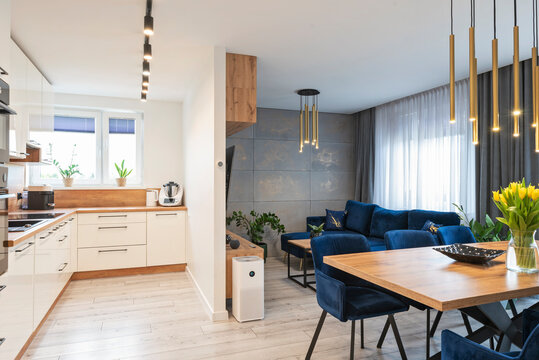 Modern dining room with kitchen and wooden table with stylish lamp over it. White furniture in new apartment and luxurious design. Home interior.