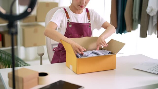 Asian women small business owner packing product clothing into shipping box preparing order for customer selling online live streaming merchant ecommerce
