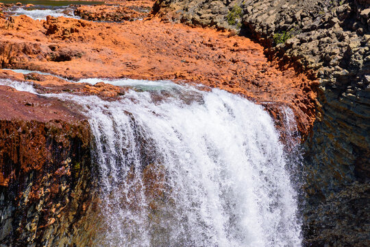 Plano medio de la ca&iacute;da de agua en la cascada Salto del Agrio, destacando el contraste entre la espuma blanca y el lecho rocoso de color &oacute;xido y azufre en la Patagonia argentina.