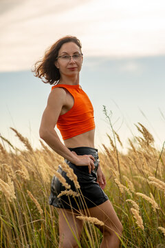 Confident Woman in Orange Crop Top and Leather Skirt in Field