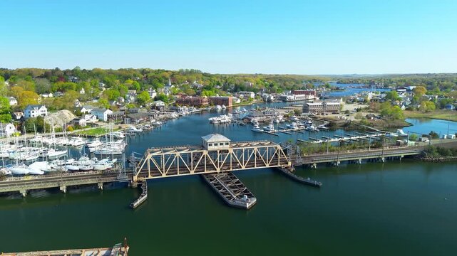 Mystic River harbor and town aerial video, a scenic drone shot tracking over boat marinas, waterfront docks, historic bridges, and historic coastal neighborhoods on a sunny day in Connecticut.