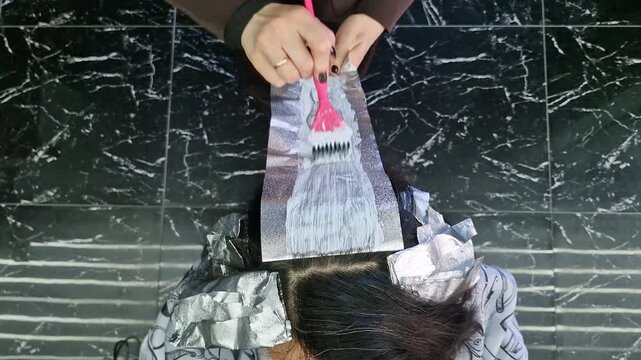 Close-up of hair lightening process. Hair strands placed on foil with blue bleaching powder applied, preparing for blonde transformation in beauty salon