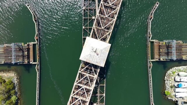 Mystic River Railroad Bridge overhead view, a high-angle aerial drone shot capturing the historic swing truss railway bridge rotating open above water and coastal boat marinas in Mystic, Connecticut.