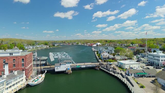 Mystic River Bascule Bridge aerial view, a high-angle drone video showing cars crossing the iconic drawbridge near downtown storefronts and the waterfront on a bright spring day in Mystic Connecticut.
