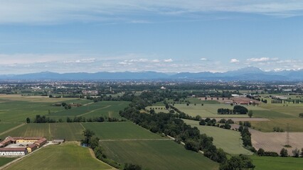 Fototapeta premium A sweeping aerial view showcases a vibrant green countryside, dotted with farms and lush fields, stretching towards a distant city skyline under a clear blue sky.