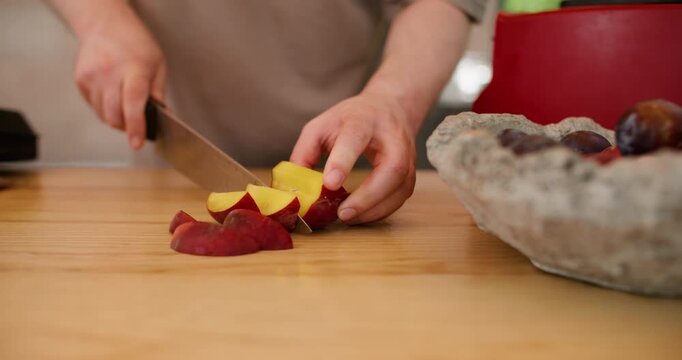 Hand cutting peach. Fruit preparation. Unrecognizable man chef using sharp knife on wooden board making peeling plums snack at workspace.