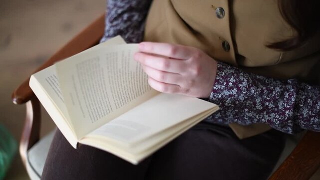 Close-up of an open book being turned by a seated person on a chair