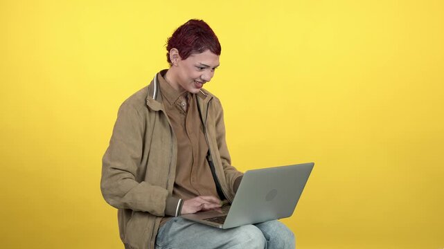 Young woman with laptop video calling on yellow background