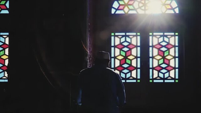 Man praying in a mosque with sunbeams through stained glass windows