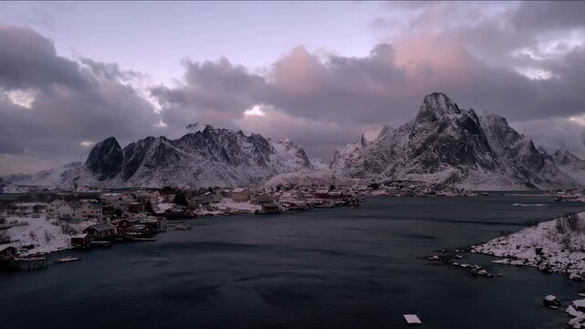 Serene winter village nestled by snow-capped mountains and dark ocean waters