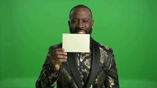 Confident Black Man in Black and Gold Brocade Blazer Smiling While Holding Blank Card Against Green Screen Background for Marketing and Compositing