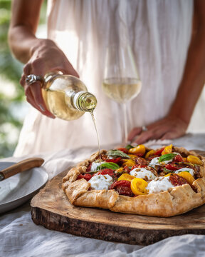 Rustikale Pizza mit frischem Gem&uuml;se und Mozzarella auf Holzbrett, dazu Wei&szlig;wein &ndash; mediterrane K&uuml;che, italienischer Genuss und sommerliches Dinner mit Copyspace