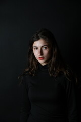 Naklejka premium Junge Frau im dunklen Rollkragenpullover vor schwarzem Hintergrund – ruhiges Fine-Art-Porträt mit melancholischer Stimmung und minimalistischer Ästhetik. Viel copyspace und copy space.