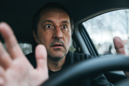 Frightened driver reacting suddenly inside car, shocked expression and raised hands in emergency situation