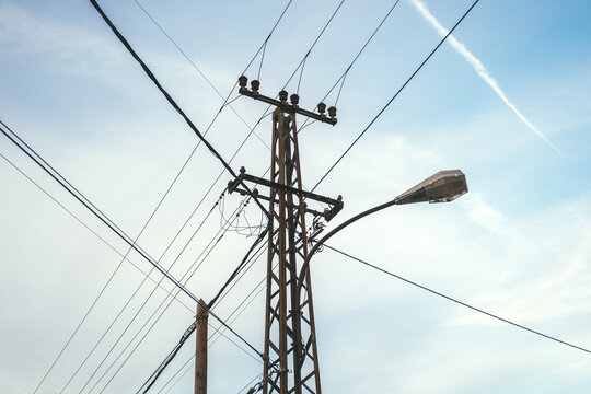 Utility pole with intersecting power lines and a curved streetlight set against a clear blue sky, illustrating urban infrastructure, overhead cables and electrical network.