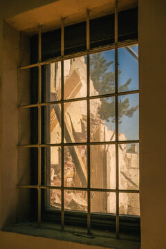 Sunlit gridded window overlooking crumbling ruins and rubble of an abandoned building