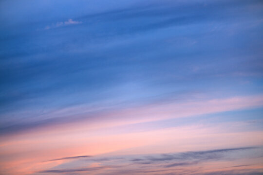 Pastel sunset sky with soft layered clouds at twilight over a calm horizon