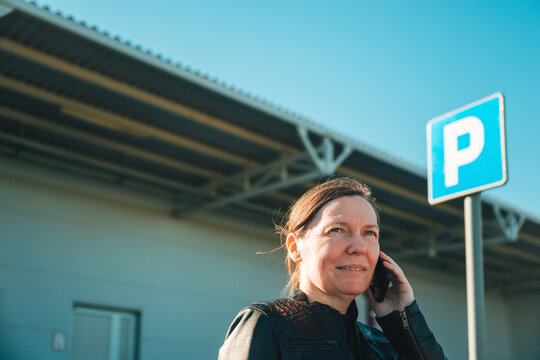 Woman talking on mobile phone by parking sign outside commercial building in daylight