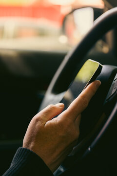 Close-up of a driver&rsquo;s hand holding a smartphone against the steering wheel inside a car