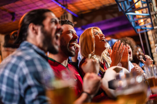 Side view of ecstatic sports fans screaming and celebrating a soccer goal in a pub.