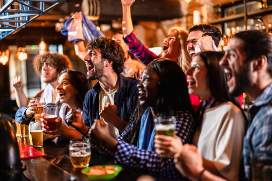 Laughing group of diverse sports fans shouting and celebrating a soccer goal in a pub.