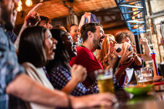 Side view of a group of excited friends celebrating a soccer goal at a pub bar counter.