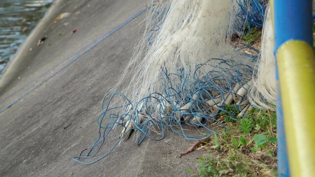 Close-up of a traditional fishing net with blue ropes and weights resting on a concrete reservoir embankment in Indonesia. Fishery equipment left to dry before the next catch.