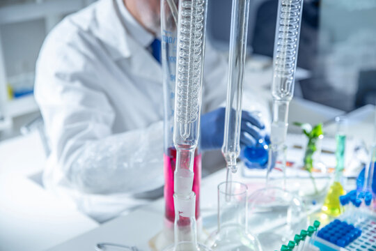 Close up of a gloved hand holding a glass rectification fractionating column among laboratory glassware. Concept for distillation, chemical engineering and analytical chemistry, copy space.