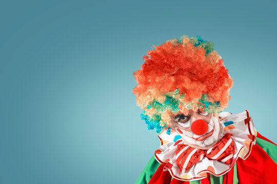 Portrait of creepy clown. Entertainer Joker in colorful suit and wig. Buffoon with clown whiteface makeup. Trickster, jester, pantomime, mime.