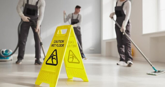 Cleaners mopping floor with janitors and safety. A bright caution sign marks wet floor as a cleaning team vacuuming and mopping the space. Concept highlights maintenance and workplace safety.