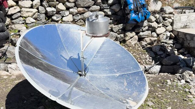 Parabolic solar cooker boiling water in metal kettle in Himalayan village