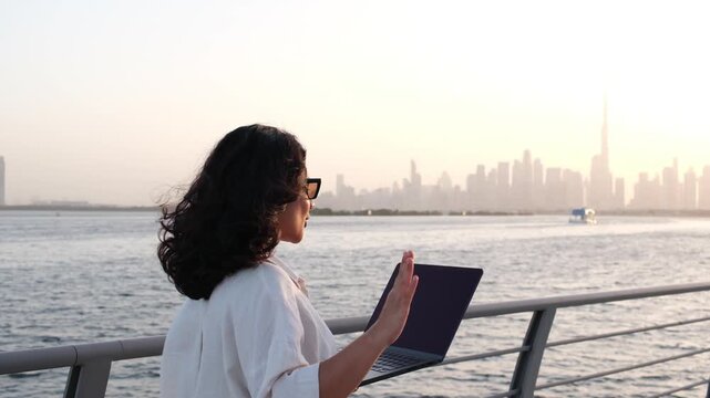 Female entrepreneur working remotely on laptop by Dubai waterfront skyline 4k video 