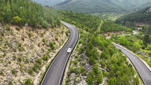 A cinematic, aesthetically pleasing drone video shot from a high angle, featuring vehicles traveling along a winding mountain road against a backdrop of lush green mountain scenery.