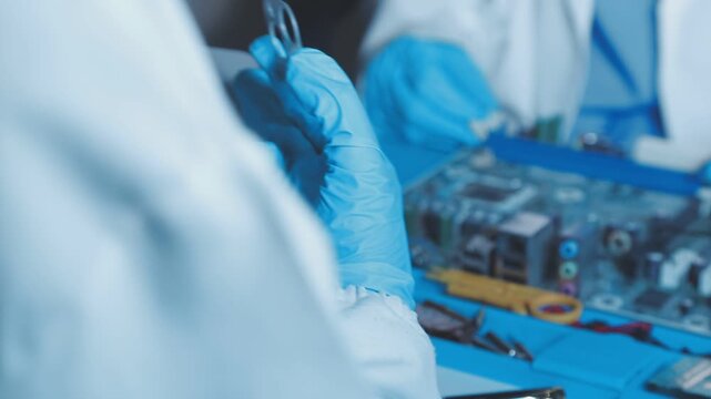 A close-up view of a technician wearing black gloves holding a computer processor chip while working on a laptop motherboard with a precision screwdriver.